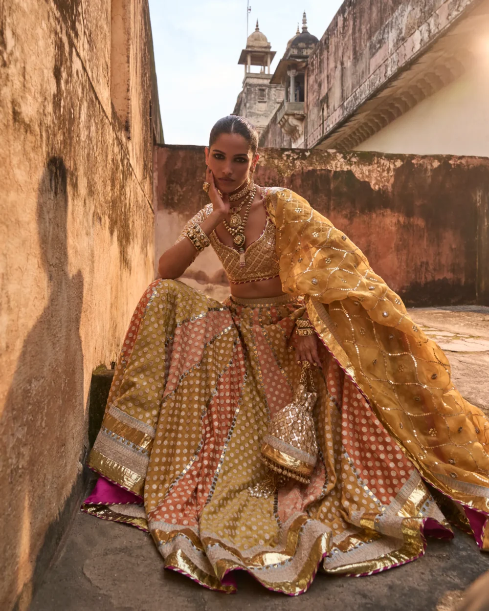 Khaddi Silk Lehenga Set featuring an orange blouse with gota work, a mustard lehenga with ari work panels, and a mustard organza dupatta. Khaddi Silk Lehenga Set featuring an orange blouse with gota work, a mustard lehenga with ari work panels, and a mustard organza dupatta.