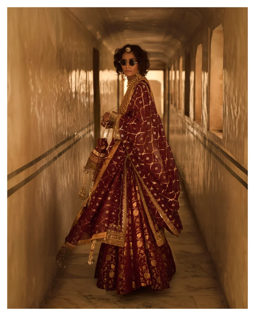 A woman gracefully poses in a stunning Maroon Jamavar Lehenga Set, exuding elegance and sophistication.