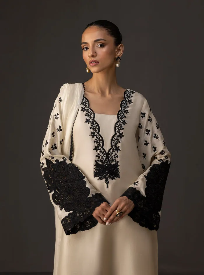 Close-up of the striking black embroidery on the neckline of the ivory embroidered shirt.ered shirt.