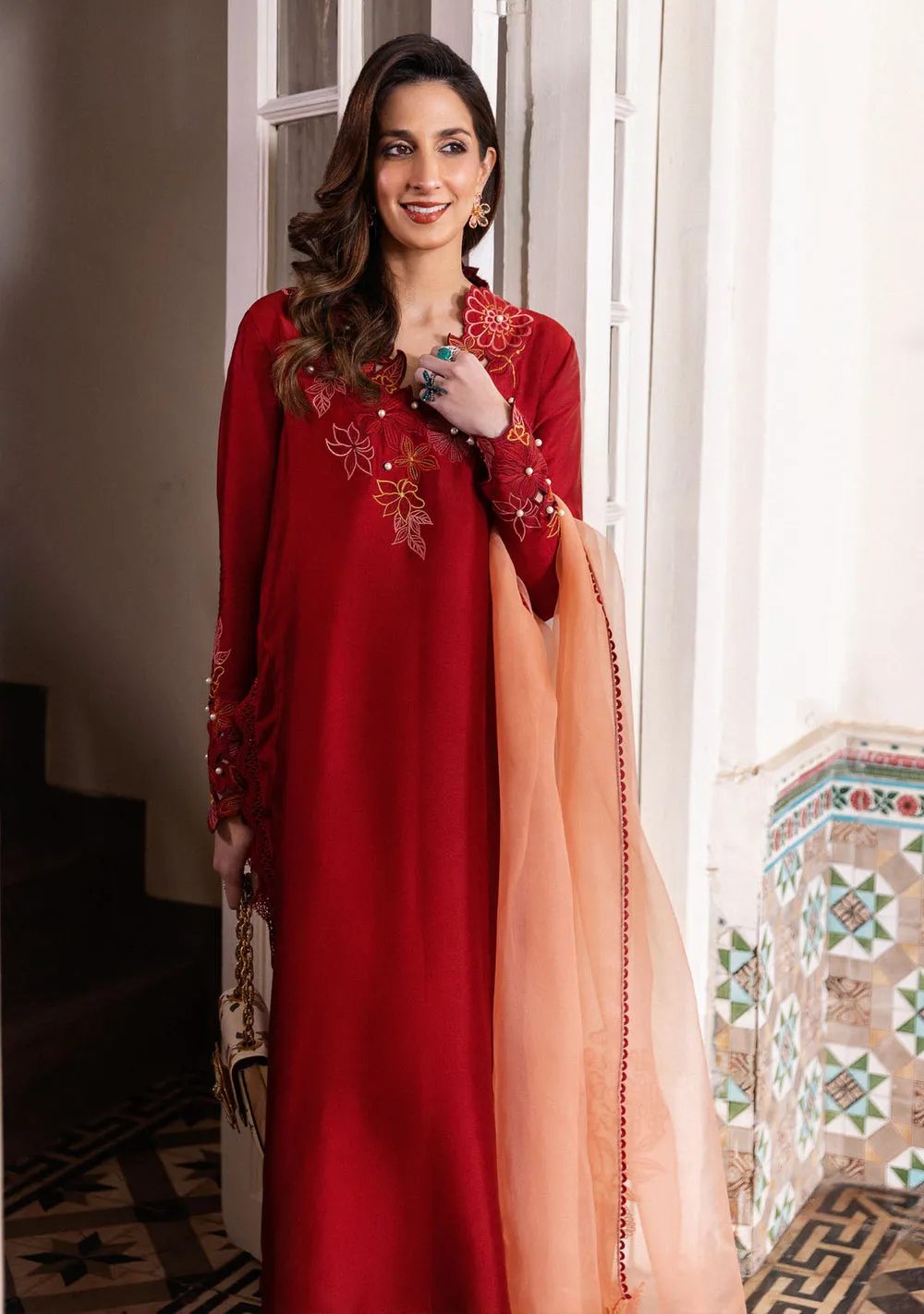 Model in brick red sheesha silk kurta and contrasting coral dupatta with asymmetrical floral embroidery for Eid.